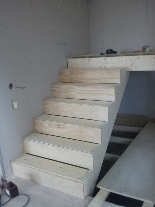 Självbyggd enkel trätrappa inomhus med synliga steg av plywood och en avstickande sista steg för komfort.