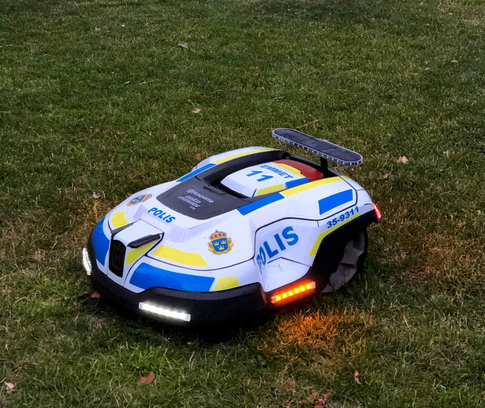 Robotgräsklippare utsmyckad som en polisbil på gräsmatta kvällstid.