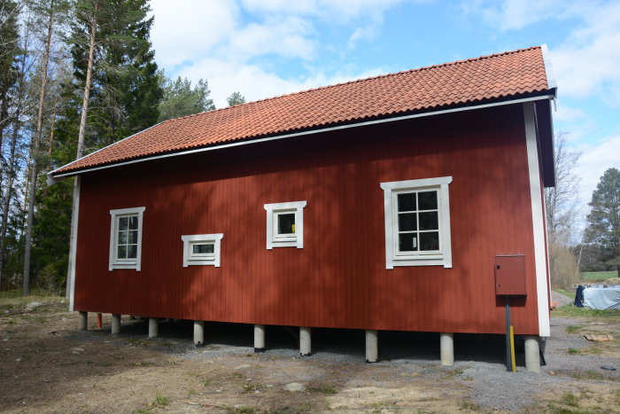 Rödfärgat hus med vita fönsterfoder och runda fönster på loft, står på betongplintar.