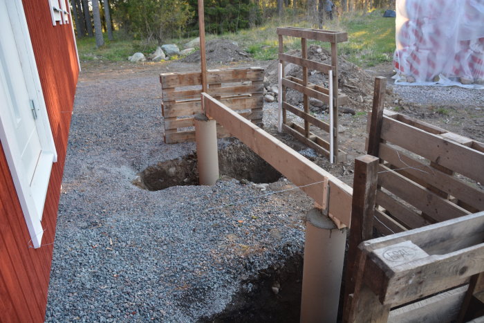 Nybyggd grund med två gjutna betongplintar vid en röd byggnad och träformar för gjutning.