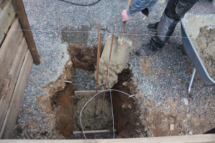 Gjutning av betongplint i grop med armeringsjärn, bredvid skottkärra med betong.