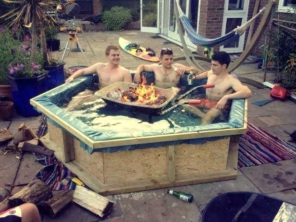 Tre män i en provisorisk hemmagjord bubbelpool med en öppen eld grill i mitten, ute på en bakgård.