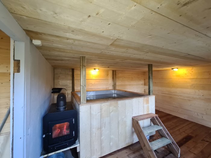 Inredning av hemmabyggt badhus med vedeldad kamin och badtunna av trä.