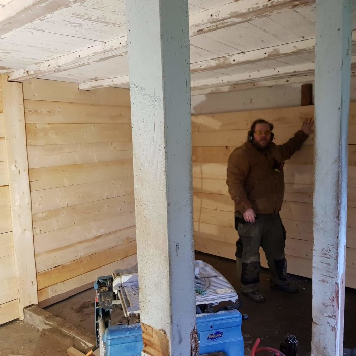Man i arbetskläder står i under renovering med träväggar och verktyg runt omkring.