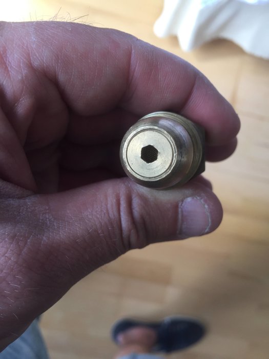 Närbild av en hand som håller en metallkoppling med en knappventil mot en trägolvbakgrund.