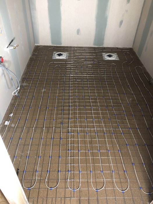Unprepped bathroom floor with installed underfloor heating system before levelling compound application.