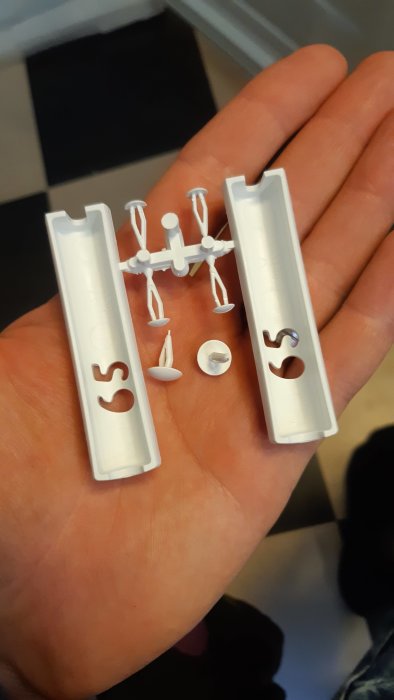 Hand håller vita plastdetaljer och fästdon från Electrolux förpackning, okänd användning.