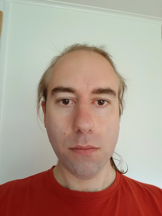 En man med halvlångt hår och röd tröja poserar för foto före trimning av skägget.