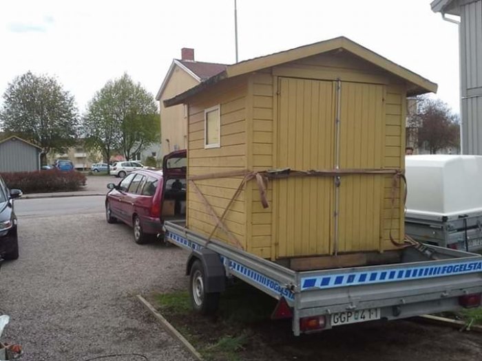 Gult skjul säkrat på en släpvagn bakom en röd bil på en parkeringsplats.