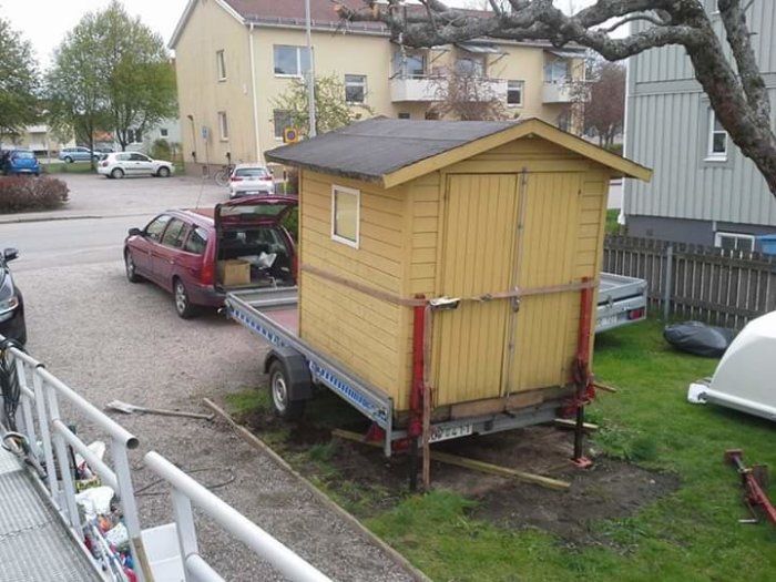 Gul stuga säkrad med spännband på släpvagn bakom bil, utan band över taket.