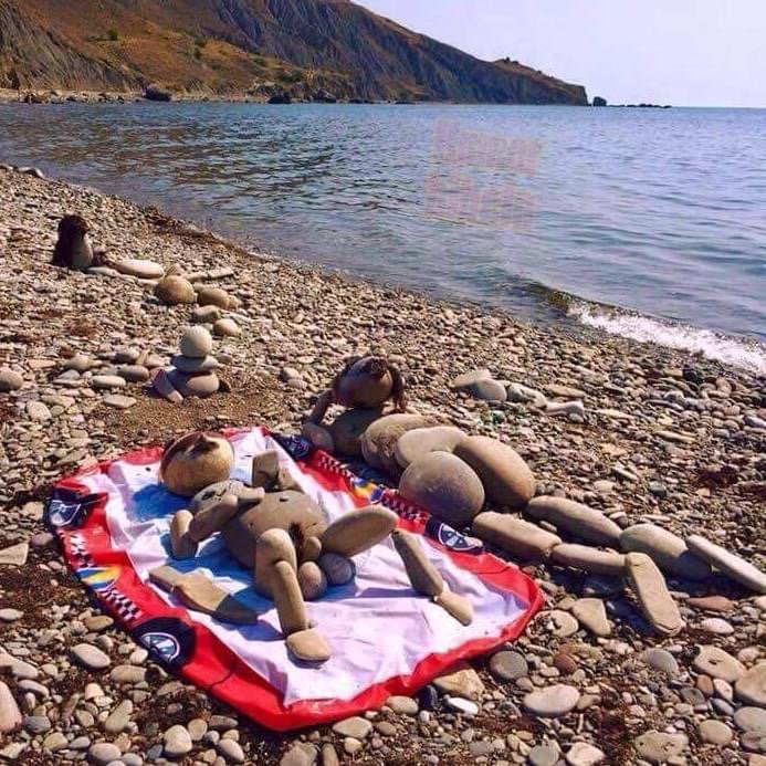 Stenfigurer ordnade på strandfilt som ger intrycket av att de solar på en grusig strand.