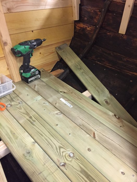 Nyinstallerade trägolvplankor i en båthytt med en grön skruvdragare och verktyg till vänster.