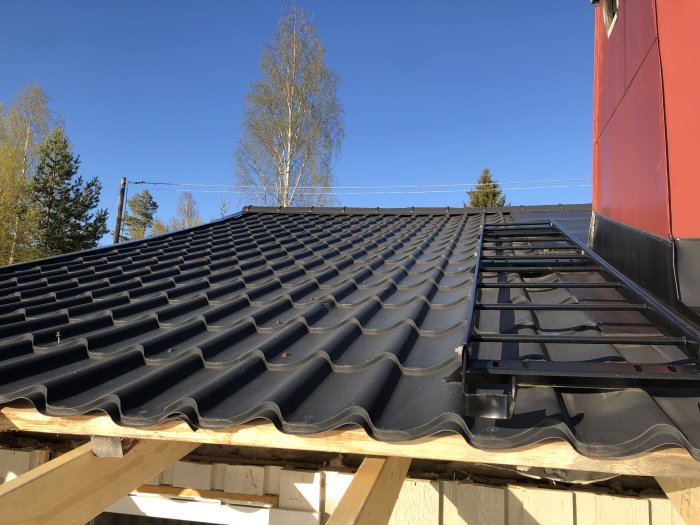 Svart, vågformad takplåt på ett hus med takstegar för säker tillgång under byggprojektet.