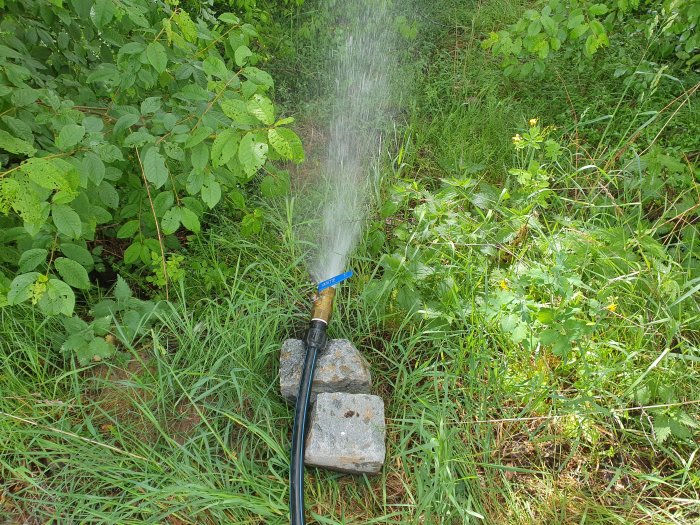 Vatten pumpas ur ny brunnen med en kulventil delvis öppen, omgiven av grönska.