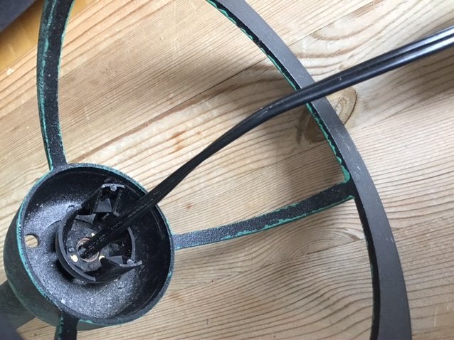 Skadad trädgårdslampa med avklippt kabel och söndermonterad sockel på ett träunderlag.
