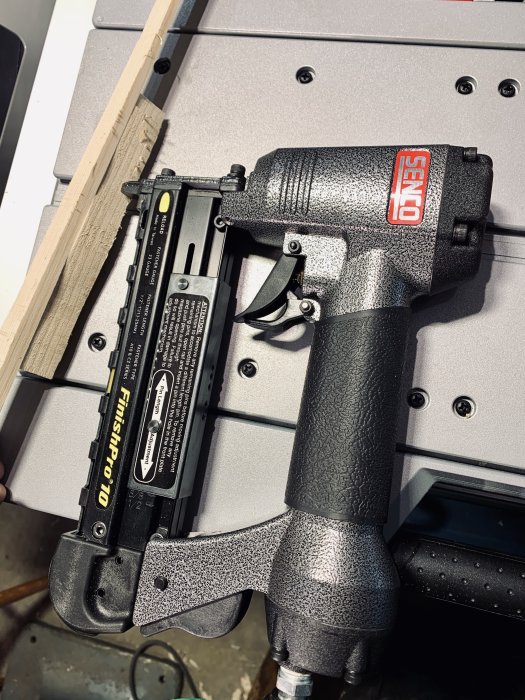 23 gauge stiftspistol vilande på verktygsbänk, skuggad textur, för små förvaringsprojekt.