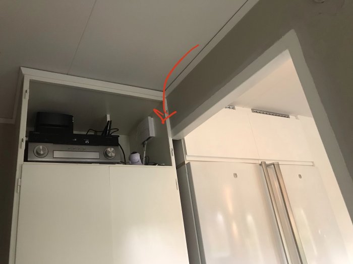 Elektronik installerad i överskåp över garderob bredvid kylskåp, röd pil markerar potentiell ventilplats.