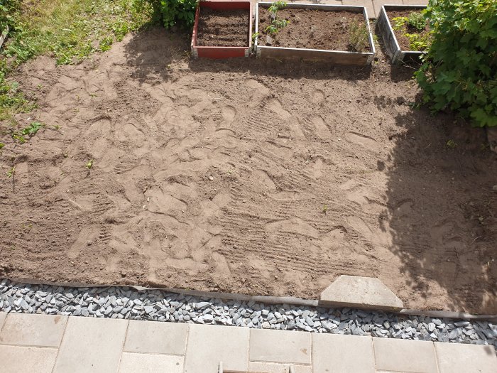 Jordyta förberedd för plantering med odlingslådor och gräsmark intill skiffersten.