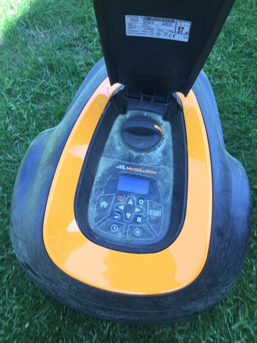 Svart och orangegul robotgräsklippare med öppen lucka som visar kontrollpanelen, på grönt gräs.