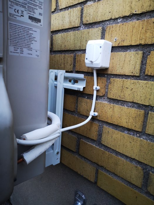 Luftvärmepumpens utomhusenhet med elkabel installation på tegelvägg.