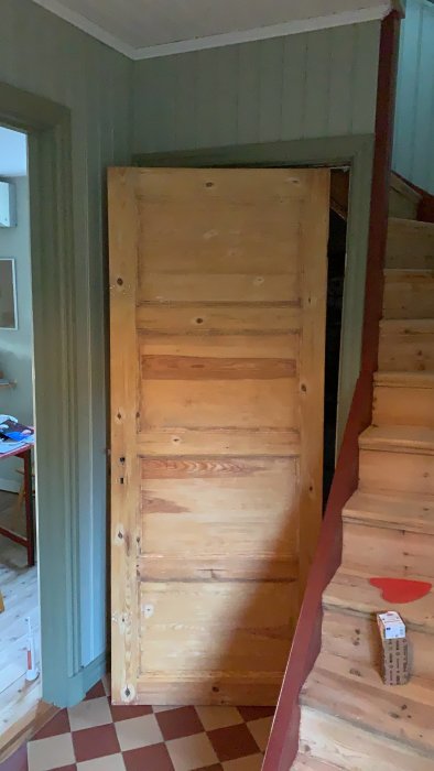 Nymålad, träfärgad källardörr i gammalt hus med trätrapp och rutigt golv.