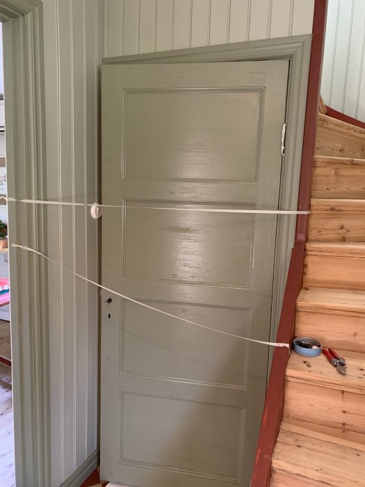 Nymålad traditionell källardörr i grågrön nyans i ett hus med synliga detaljer och verktyg.