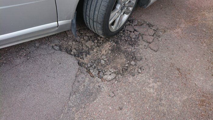 Skadad asfalt på garageuppfart med lossnade bitar intill en bildäck.