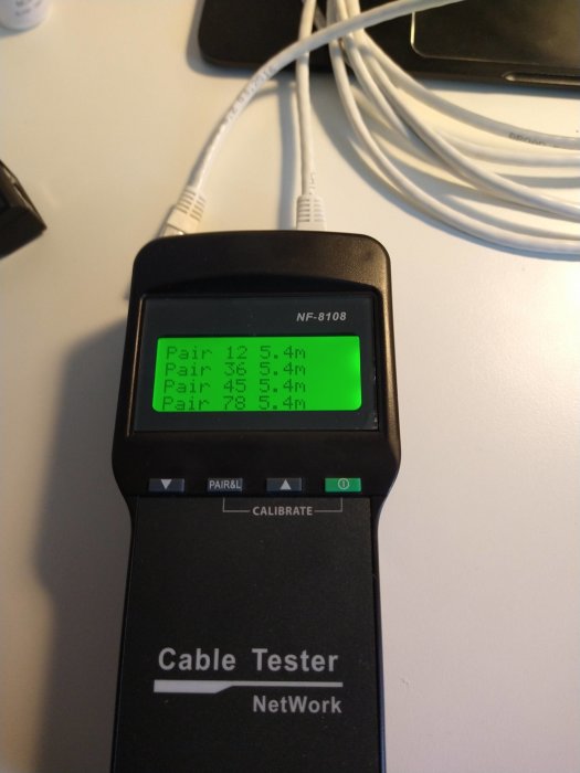 Nätverkskabelns tester med display som visar längden på fyra par trådar, varierar mellan 5.4m, ansluten till en vit nätverkskabel.