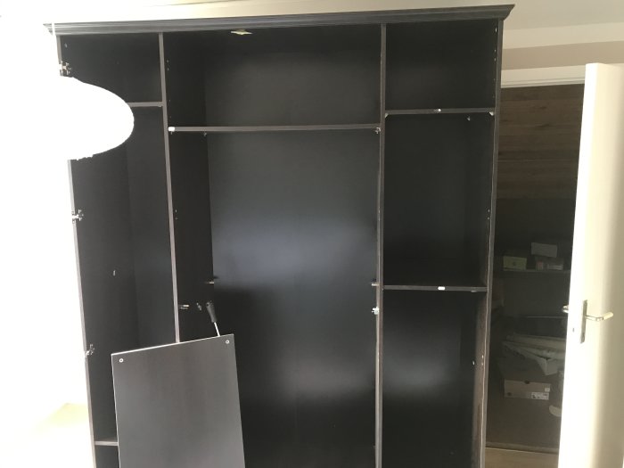 Delvis ihopskruvat svart skåp bredvid öppen dörr, påbörjad walk-in-closet.