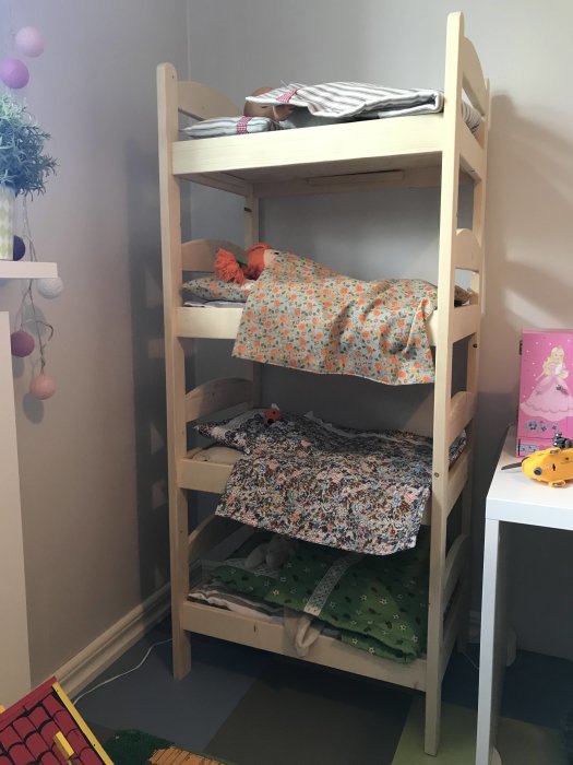 Hemmagjord fyrvåningsdocksäng av panelvirke med färgglada sängkläder i barnrum.