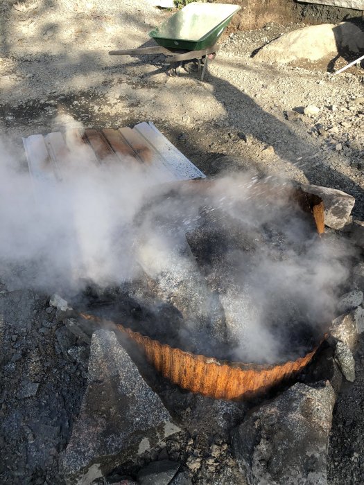 Rostig plåt täcker en häll som bryts av eldning, med synlig rök och en skottkärra i bakgrunden.