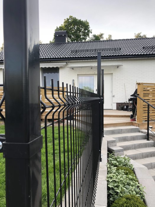 Nymonterad kortsida av svart staket i 3D-design framför vit villa med uppfräschad gräsmatta.