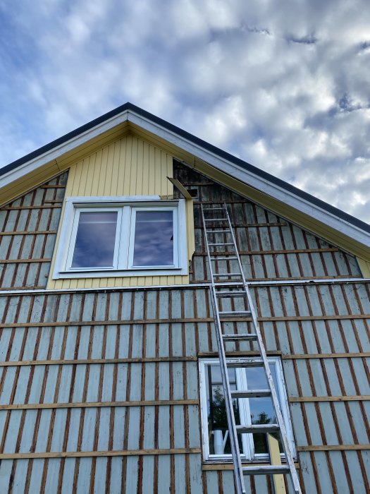 Husvägg under renovering med träpanel delvis avlägsnad och synligt mögel på övre delen.