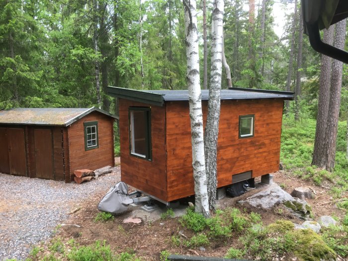 Nyrenoverat stugtak med vindskivor, brunmålad träfasad, och stort fönster i linje med ytterväggen, omgivet av skog.