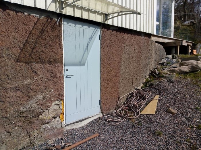 En delvis putsad husmur med en källardörr, där höger sida ser intakt ut, redo för putsarbeten.