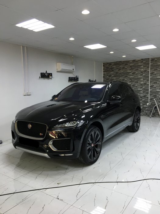 En svart Jaguar F-Pace parkerad i ett rent garage med marmorliknande golv och stenvägg.