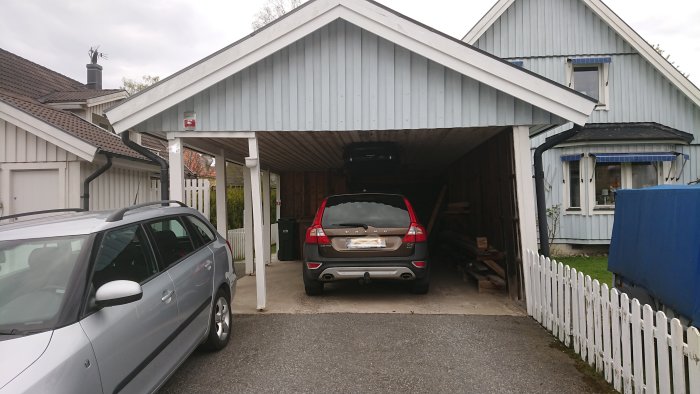 Carport på sned med bil inuti, bredvid hus, visar konstruktionens skevhet.