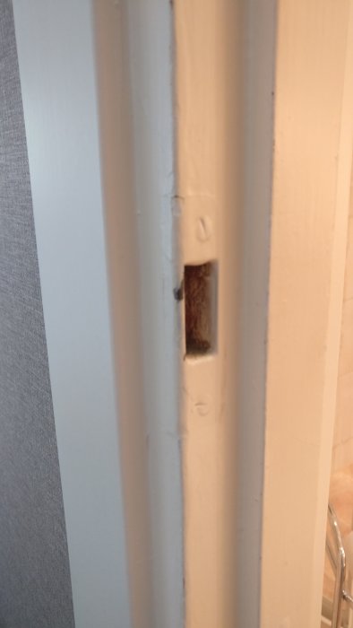 Vit innerdörrkarm med slitage och en synlig låsmekanism, vilket kan orsaka problem med att stänga dörren.