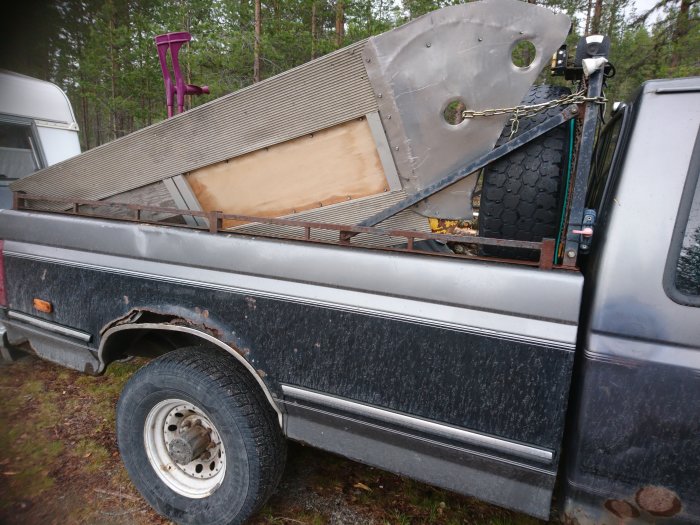 En lastbilslåda med varierade objekt surrade med kedja, inklusive en metallramp och däck.