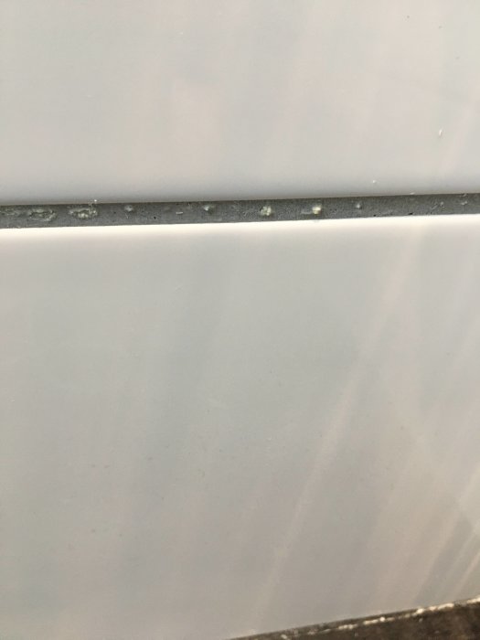 Vitt pulveraktigt avlagring på kakelfogen ovanför en kakelplatta i badrum.