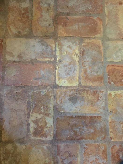 Handslaget tegelgolv med varierande rödbruna toner och synlig slitage i en äldre bostad.