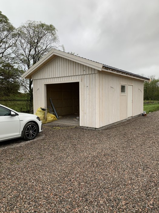 Halvfärdigt garagebygge på 8x4,5 meter med öppen port och vitklädd fasad, framför en vit bil.