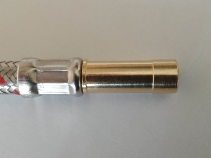 Närbild av en krananslutning med ett stelt kopparrör och en flätad flexibel del, mot en neutral bakgrund.