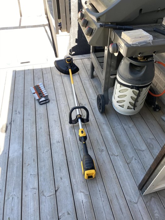 Ny Dewalt batteridriven kantklippare med gula och svarta detaljer på en träveranda intill grill och borrskruvdragare.