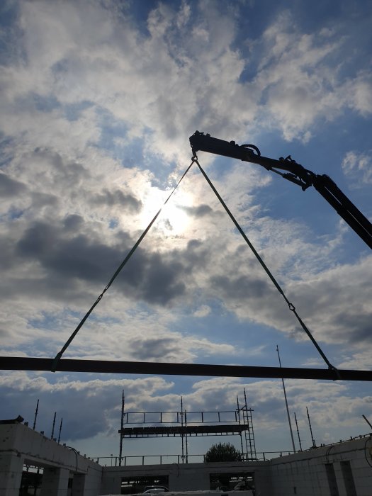 Installation av takstol med kran mot molnig himmel över byggplats med väggar och ställningar.