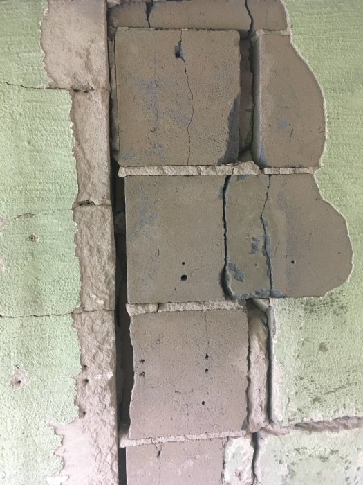 Skadade och spruckna betongblock i en vägg med synlig spricka och lossande sektioner.