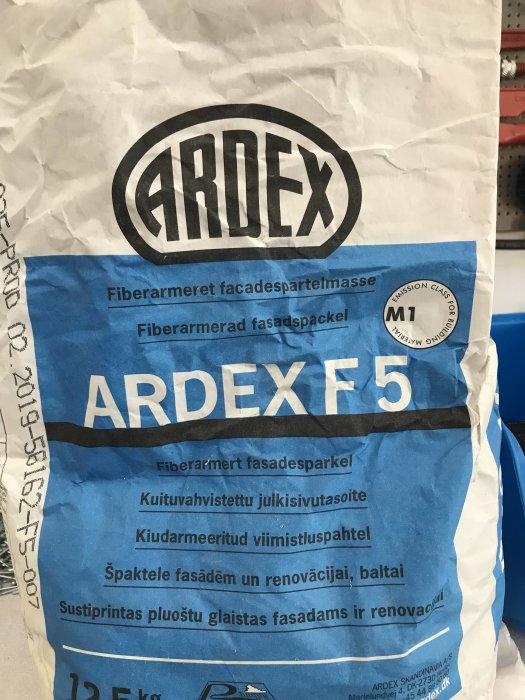 Säck av ARDEX F5 fiberarmerad fasadspackel framför byggmaterialhyllor.