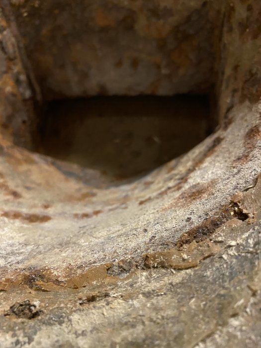 Närbild på en gammal och rostig installation som kan vara en golvbrunn eller spygatt i en betongyta.