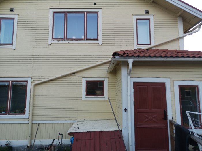 Gult tvåvåningshus med röda fönsterkarmar och snedtak visar exteriör och fasad.