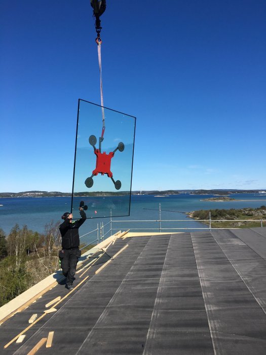 Installation av stort fönster med sugkoppslyft på hustak vid havet.